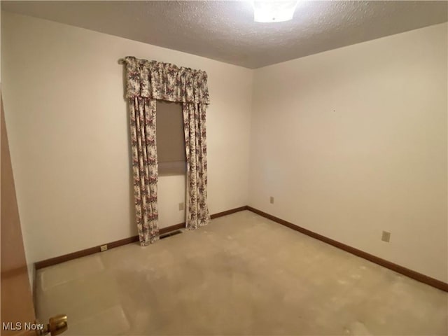 empty room with light carpet, a textured ceiling, and baseboards