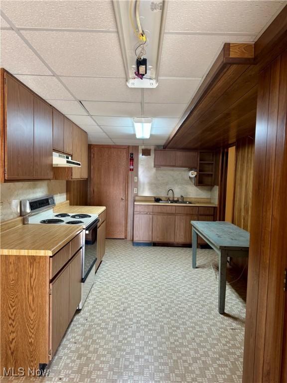 kitchen with under cabinet range hood, wood walls, range with electric cooktop, light countertops, and light floors