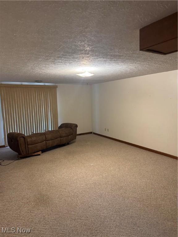 unfurnished living room featuring carpet flooring, a textured ceiling, and baseboards