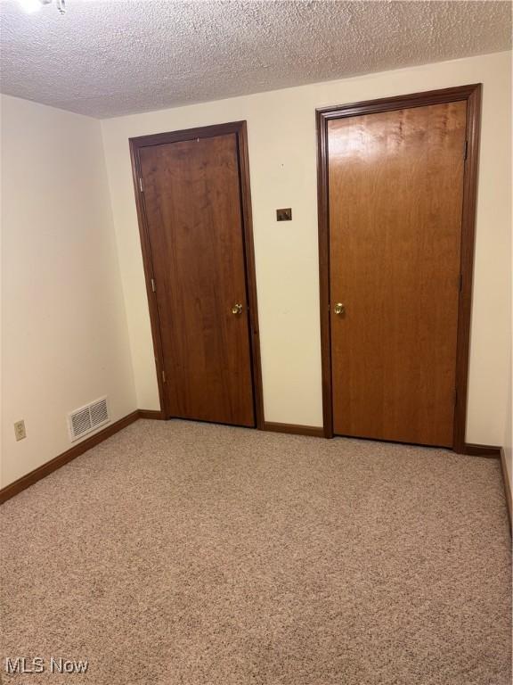 unfurnished bedroom featuring light carpet, baseboards, visible vents, and a textured ceiling