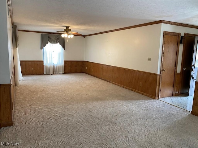 carpeted spare room featuring wood walls, a ceiling fan, a textured ceiling, and wainscoting