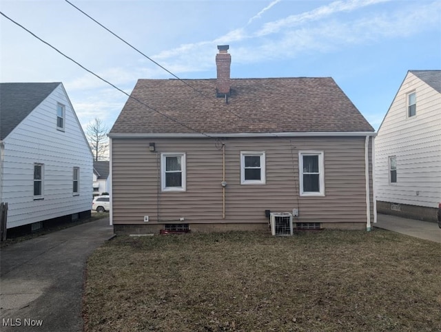 rear view of property featuring roof with shingles, a chimney, cooling unit, and a yard