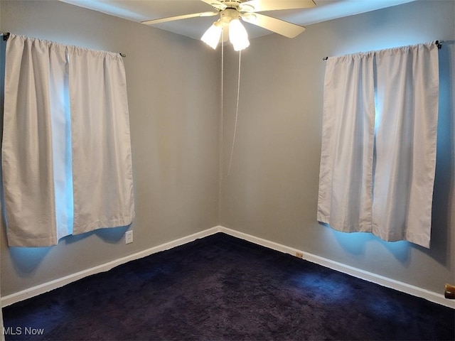 spare room with ceiling fan, dark colored carpet, and baseboards