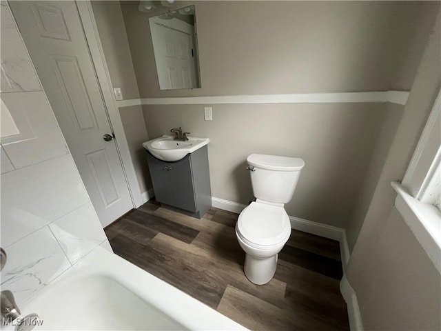 bathroom featuring toilet, baseboards, wood finished floors, and vanity