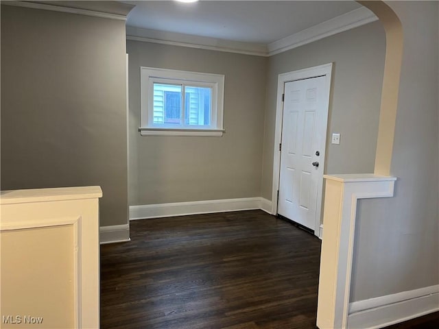 foyer entrance featuring arched walkways, ornamental molding, dark wood-style flooring, and baseboards