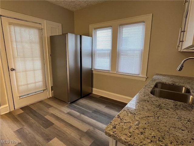 kitchen featuring light stone counters, dark wood-style flooring, freestanding refrigerator, a sink, and a textured ceiling