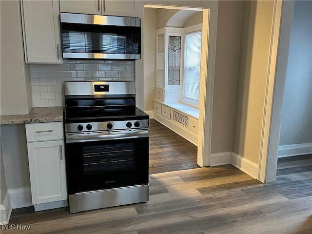 kitchen with dark wood finished floors, backsplash, appliances with stainless steel finishes, white cabinetry, and baseboards