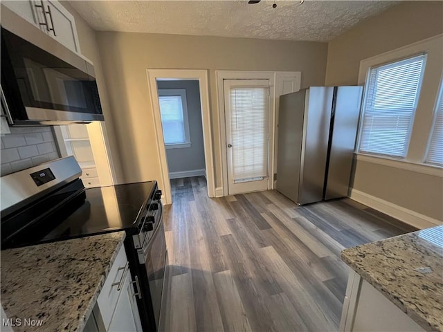 kitchen with baseboards, decorative backsplash, wood finished floors, stainless steel appliances, and a textured ceiling