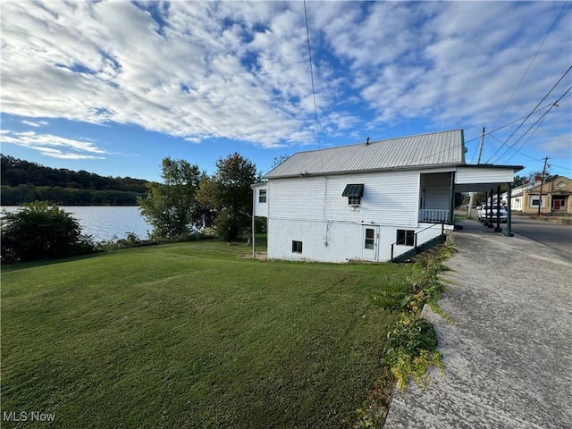 view of side of property featuring driveway, metal roof, an attached carport, a water view, and a yard