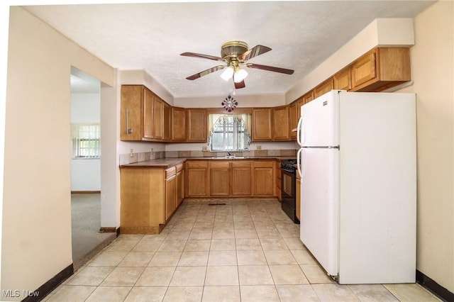 kitchen with a sink, a ceiling fan, black range with gas stovetop, freestanding refrigerator, and brown cabinetry