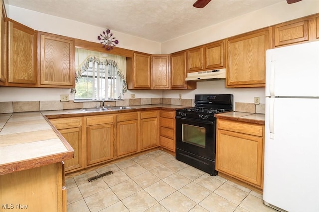 kitchen with black range with gas cooktop, a ceiling fan, freestanding refrigerator, under cabinet range hood, and a sink