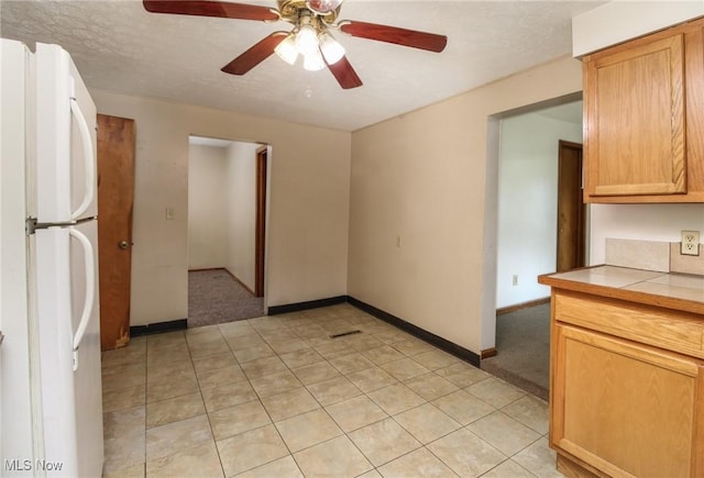 kitchen featuring baseboards, tile countertops, freestanding refrigerator, a textured ceiling, and light tile patterned flooring