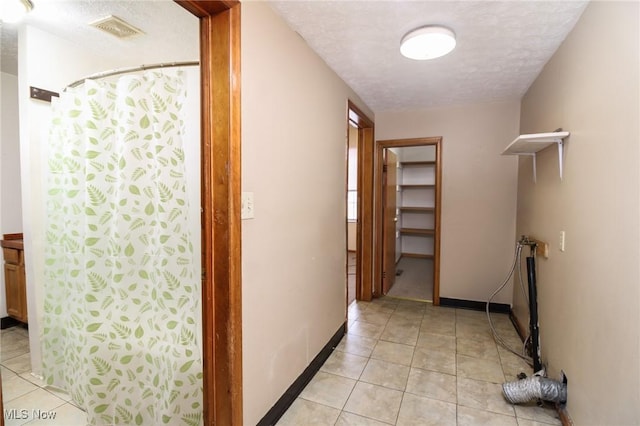 hallway featuring light tile patterned floors, a textured ceiling, visible vents, and baseboards