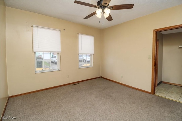 spare room with light carpet, ceiling fan, visible vents, and baseboards