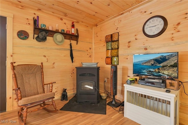 living area featuring a wood stove, wooden ceiling, wooden walls, and wood finished floors