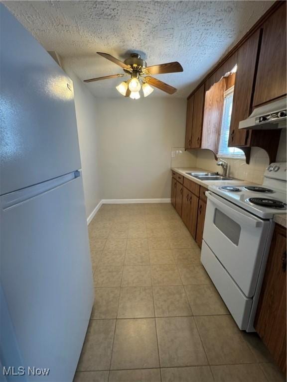 kitchen featuring a sink, a textured ceiling, white appliances, under cabinet range hood, and baseboards