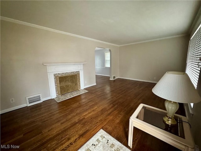 unfurnished living room with arched walkways, wood finished floors, visible vents, baseboards, and a tiled fireplace