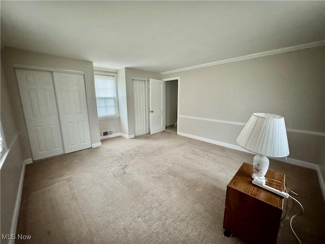 unfurnished bedroom featuring baseboards, visible vents, ornamental molding, carpet floors, and two closets