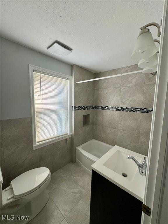 full bath featuring tile walls, toilet, washtub / shower combination, vanity, and a textured ceiling