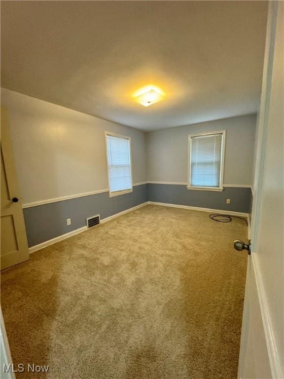 spare room featuring carpet, visible vents, and baseboards