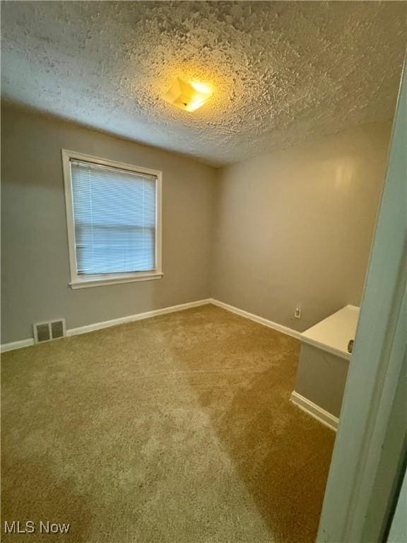 spare room featuring baseboards, carpet, visible vents, and a textured ceiling