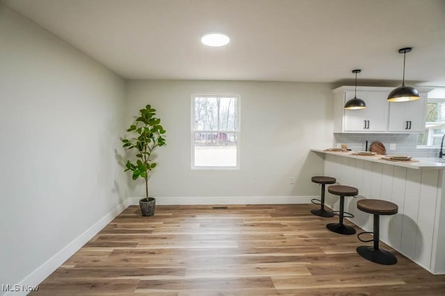 kitchen featuring tasteful backsplash, light countertops, light wood-style flooring, a kitchen breakfast bar, and baseboards