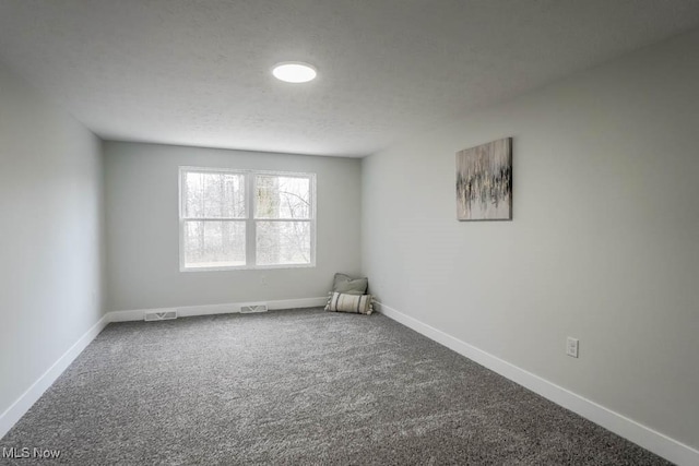 empty room with a textured ceiling, carpet flooring, visible vents, and baseboards