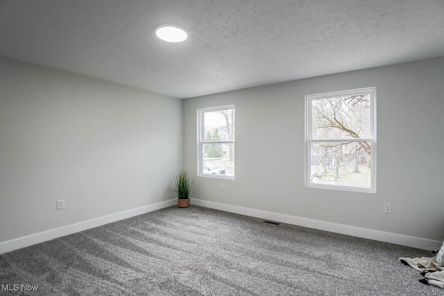 unfurnished room featuring a textured ceiling, carpet flooring, visible vents, and baseboards