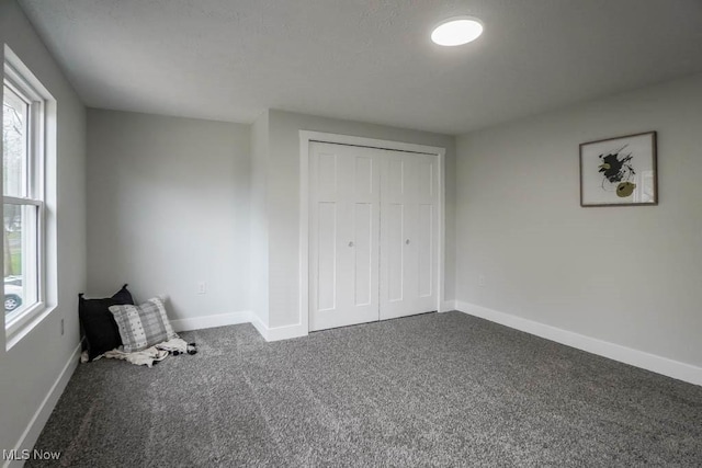 unfurnished bedroom with dark colored carpet, a closet, and baseboards