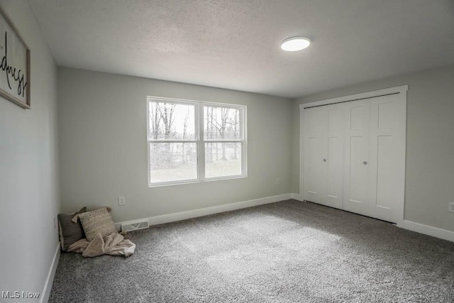 unfurnished bedroom featuring carpet, visible vents, a textured ceiling, and baseboards