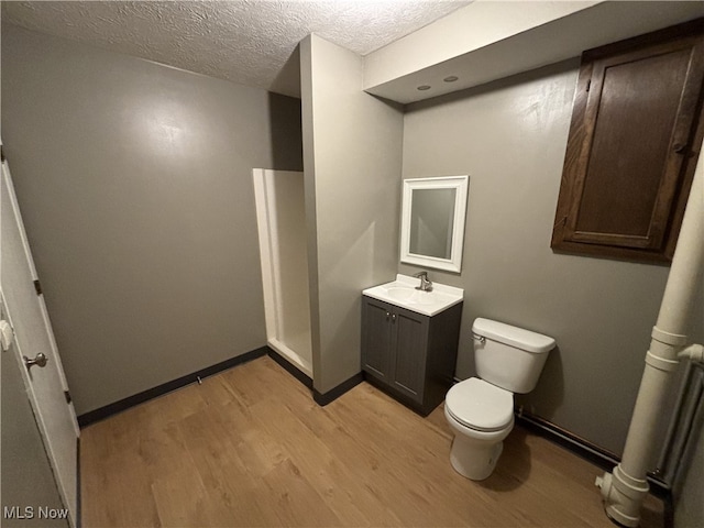 bathroom with a textured ceiling, toilet, wood finished floors, vanity, and baseboards