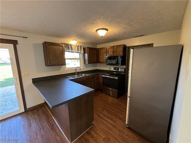 kitchen featuring a peninsula, a sink, appliances with stainless steel finishes, dark countertops, and dark wood finished floors