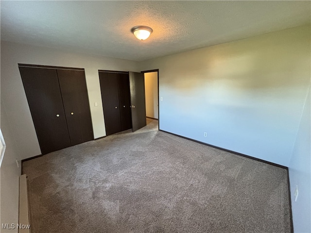 unfurnished bedroom with a textured ceiling, baseboards, carpet flooring, and multiple closets