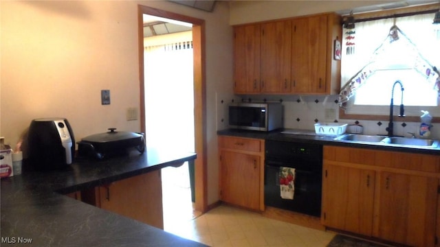 kitchen with tasteful backsplash, dark countertops, stainless steel microwave, a sink, and dishwashing machine