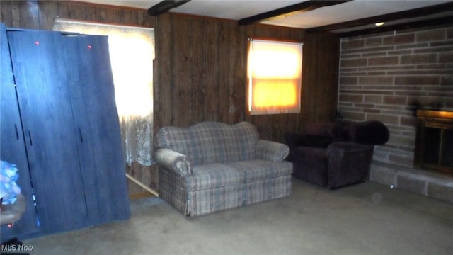 living area featuring a fireplace with raised hearth, wood walls, and beam ceiling