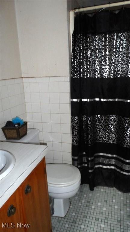 bathroom featuring tile walls, curtained shower, toilet, vanity, and tile patterned floors