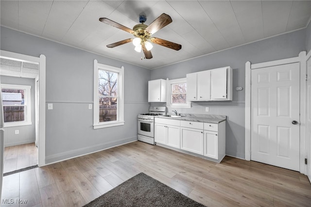 kitchen featuring a sink, light wood-style flooring, white cabinetry, and gas range gas stove