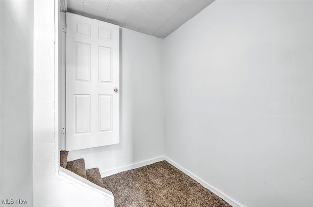 carpeted empty room featuring baseboards and stairs