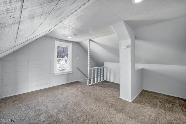 additional living space with carpet floors, baseboards, vaulted ceiling, and a textured ceiling