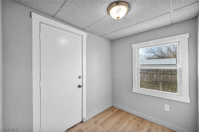 spare room featuring light wood-style floors, a paneled ceiling, and baseboards