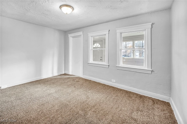 carpeted empty room featuring a textured ceiling and baseboards