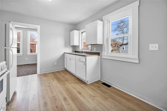 kitchen featuring white appliances, visible vents, light wood-style floors, white cabinetry, and a sink