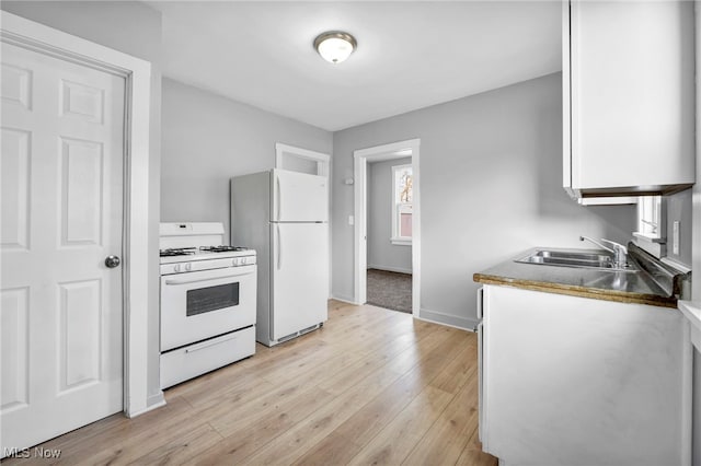 kitchen with white appliances, baseboards, white cabinets, light wood-style flooring, and a sink