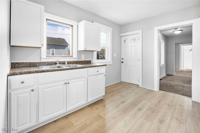 kitchen featuring a sink, baseboards, white cabinets, light wood-type flooring, and dark countertops