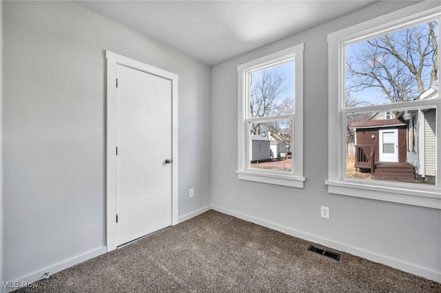 spare room with carpet floors, visible vents, and baseboards