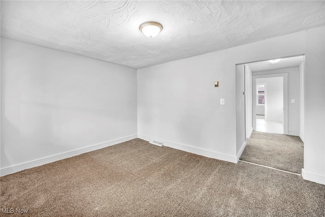 empty room with carpet floors, visible vents, baseboards, and a textured ceiling