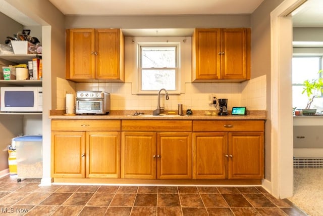 kitchen with white microwave, backsplash, a sink, and a healthy amount of sunlight