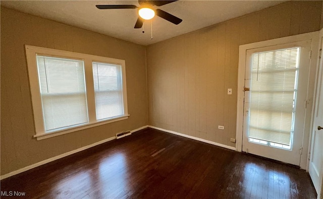 spare room with dark wood-type flooring, visible vents, ceiling fan, and baseboards