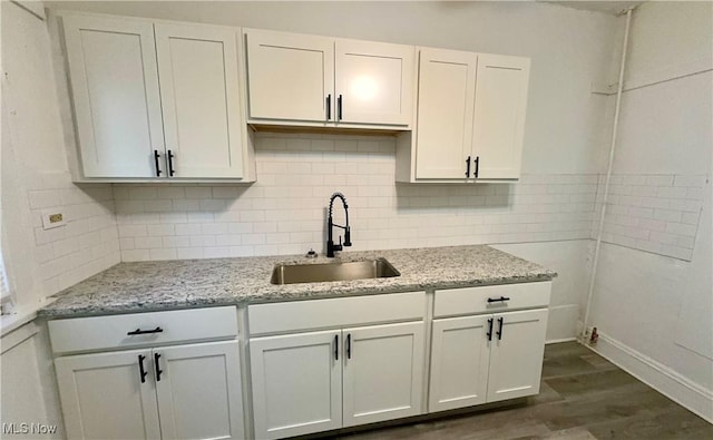 kitchen with white cabinets, dark wood-type flooring, a sink, light stone countertops, and backsplash