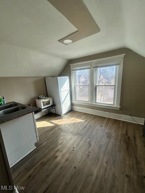 additional living space with lofted ceiling, dark wood-type flooring, a sink, and baseboards